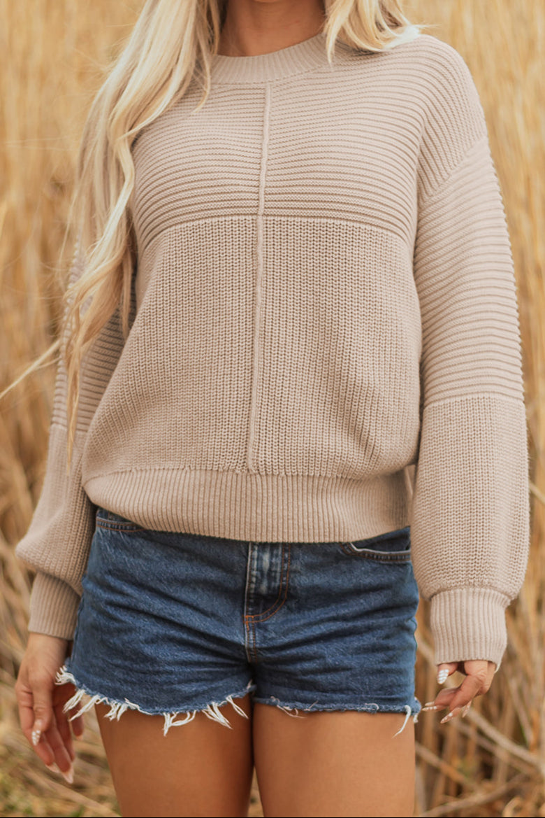 Person wearing a beige sweater and denim shorts in a field