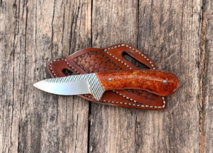 Knife with a brown handle and leather sheath on a wooden surface