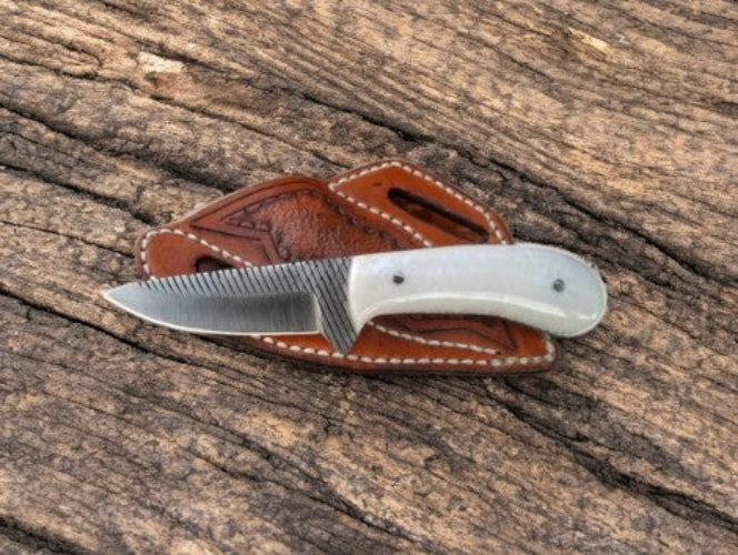 Fixed knife with white handle on a brown leather sheath on a wooden surface