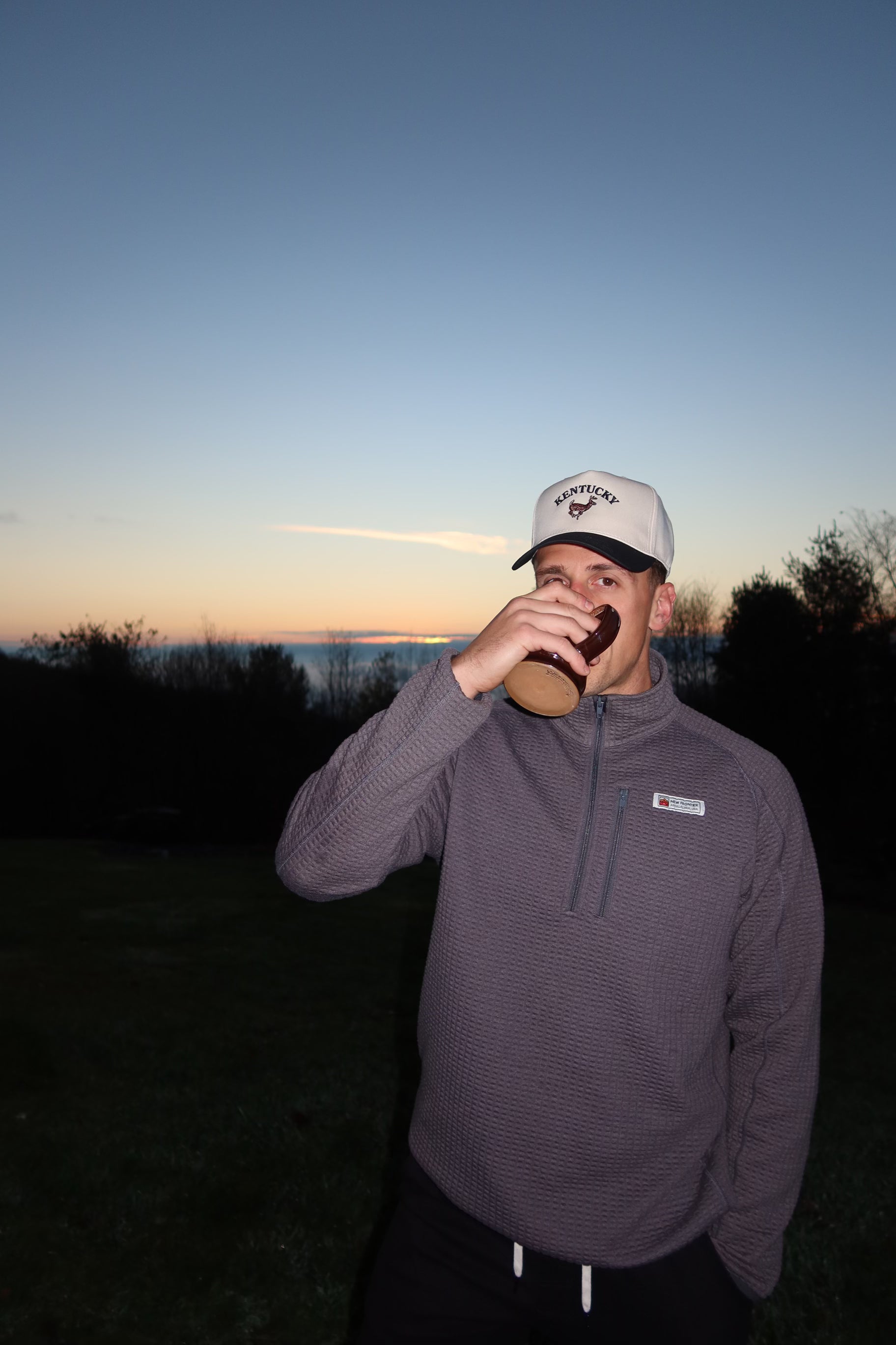 Person drinking from a wooden cup outdoors at sunset
