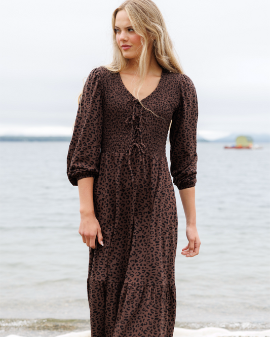 Woman wearing a brown leopard print dress standing on a beach.