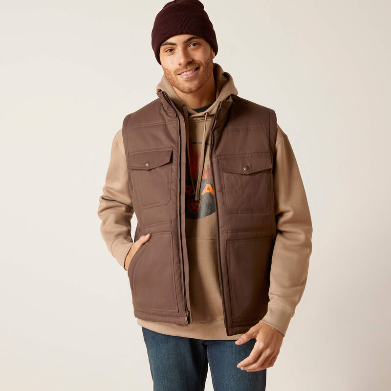 Man wearing a brown vest over a beige shirt with a plain background