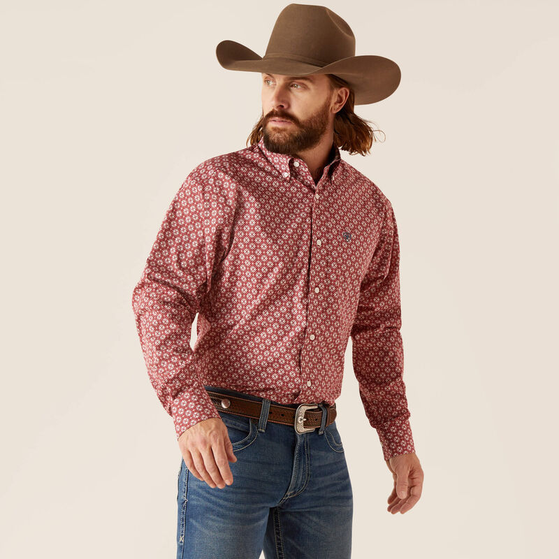 Man wearing a red patterned shirt, blue jeans, and a brown cowboy hat on a beige background