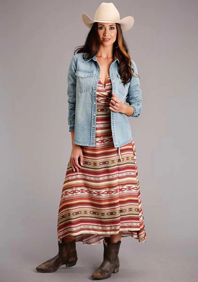 Woman wearing a long striped dress, denim jacket, and cowboy hat on a gray background