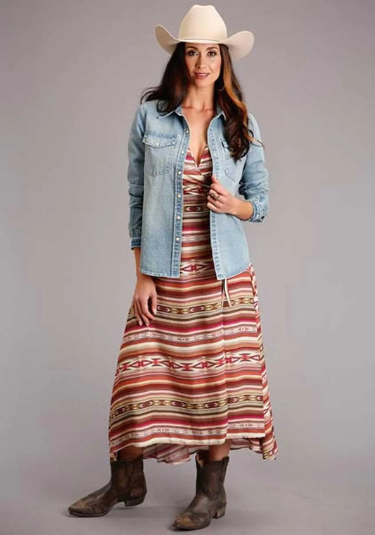 Woman wearing a long striped dress, denim jacket, and cowboy hat on a gray background