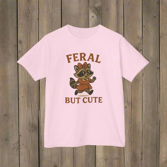 Pink t-shirt with a raccoon graphic and text 'Feral But Cute' on a white background