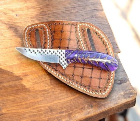Knife with purple handle in a brown leather sheath on a wooden surface