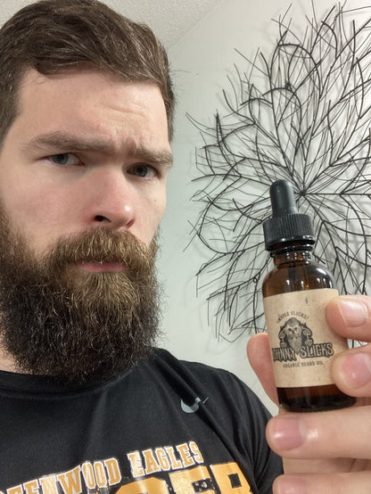 Man holding a bottle of 'Benna & Slokes' organic beard oil with a decorative wall in the background.