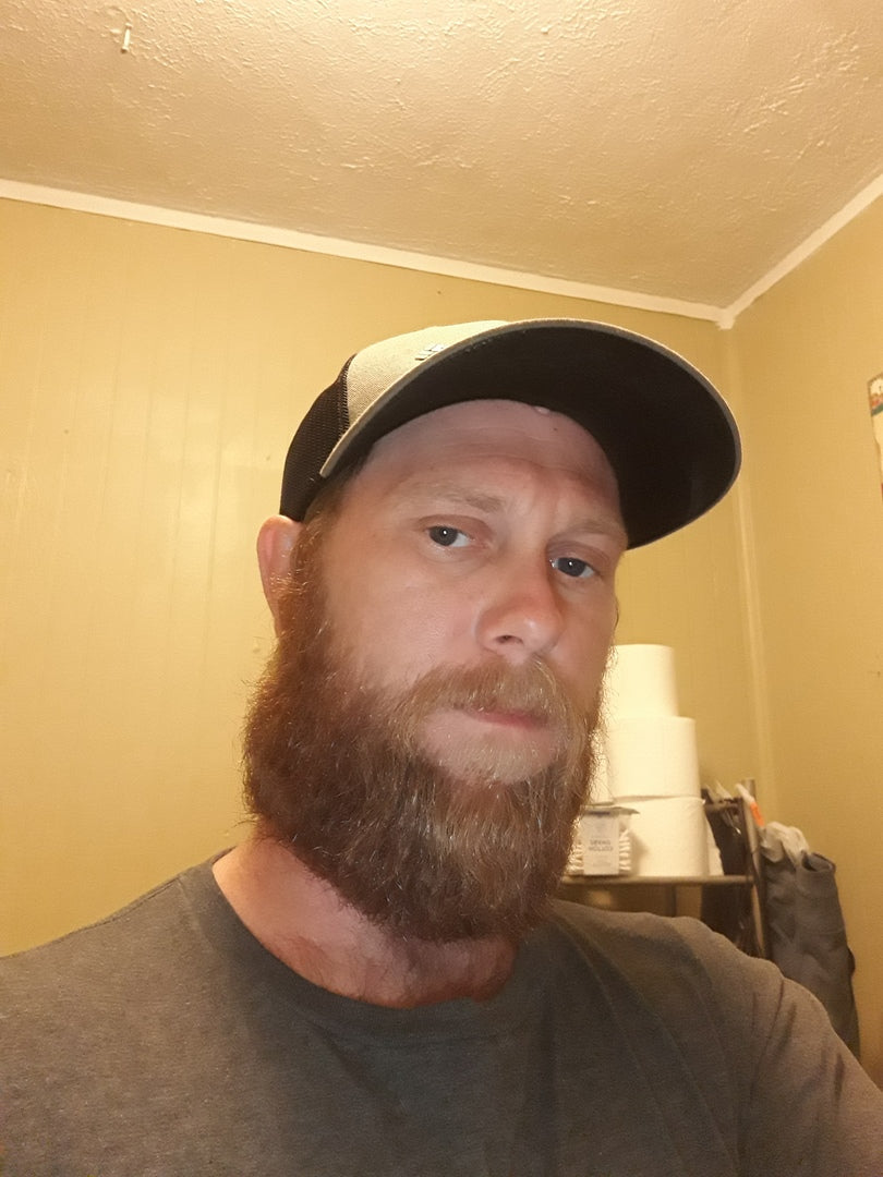 Man with a beard wearing a cap indoors against a beige wall.
