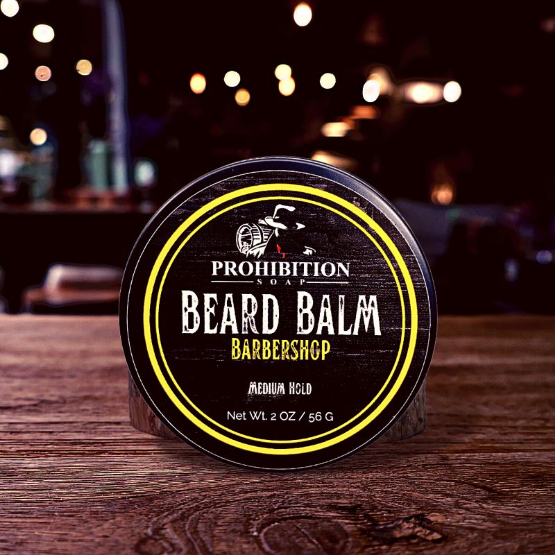 Prohibition Soap Barber Shop Beard balm container on a wooden surface with blurred lights in the background