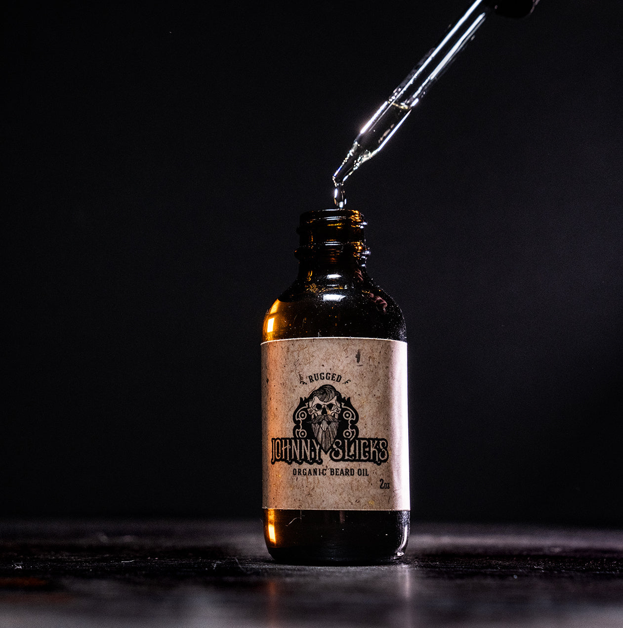 Bottle of Johnny Slicks organic beard oil with a dropper on a dark background