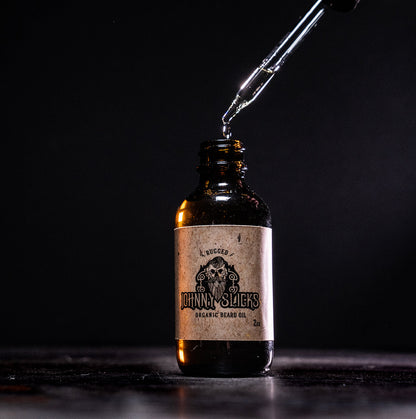 Bottle of Johnny Slicks organic beard oil with a dropper on a dark background