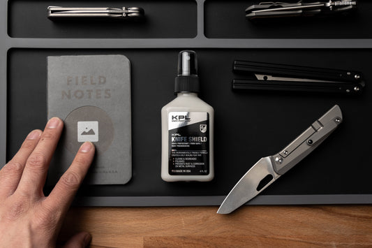 Desk with field notes, KPL Knife Shield, and knife on a black surface