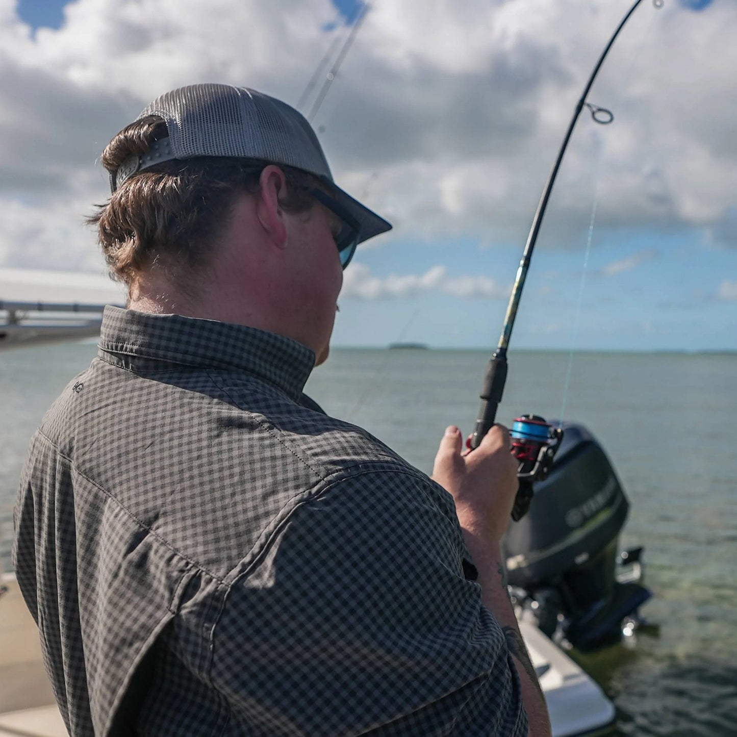 Person fishing on a boat with a cloudy sky and water background
