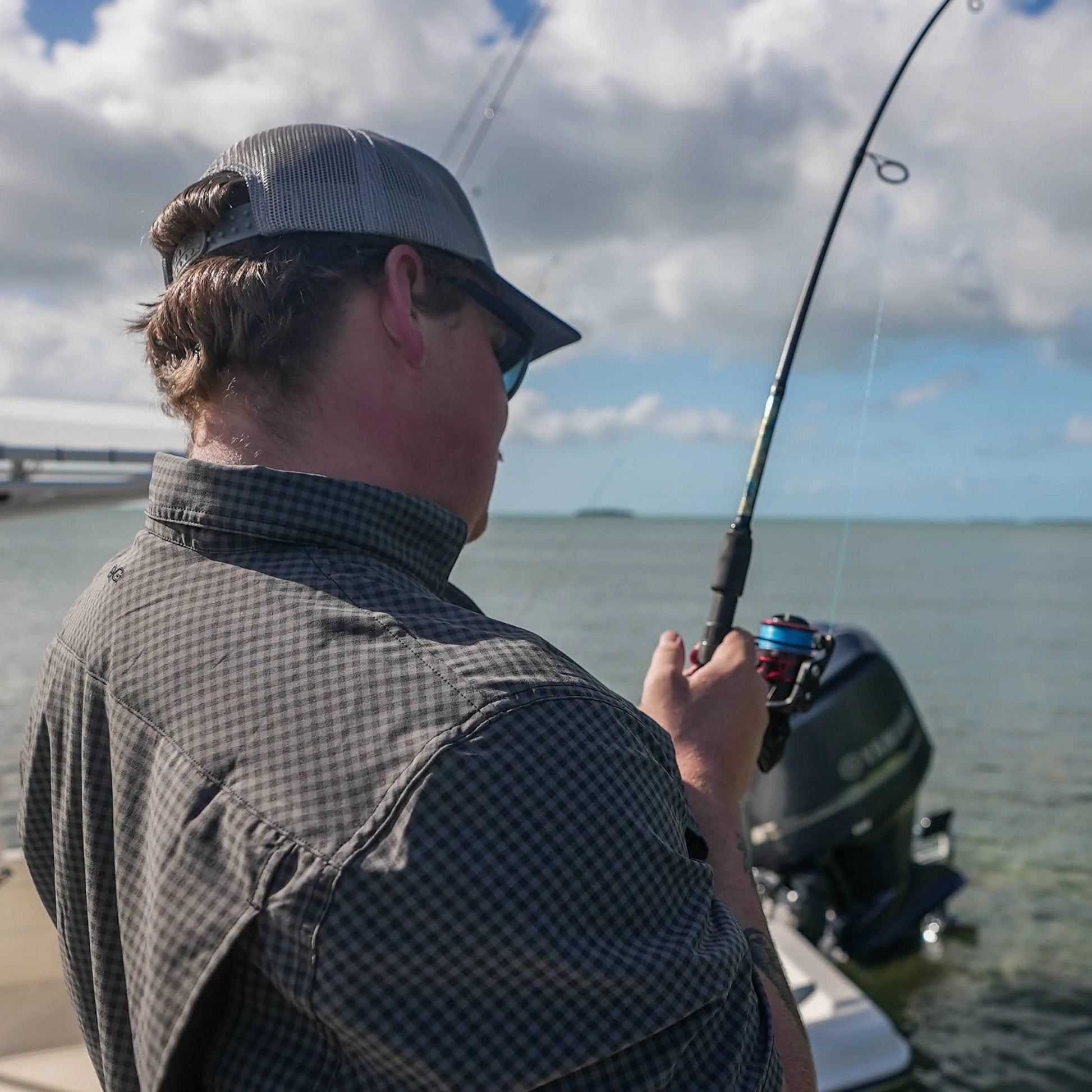 Person fishing on a boat with a cloudy sky and water background