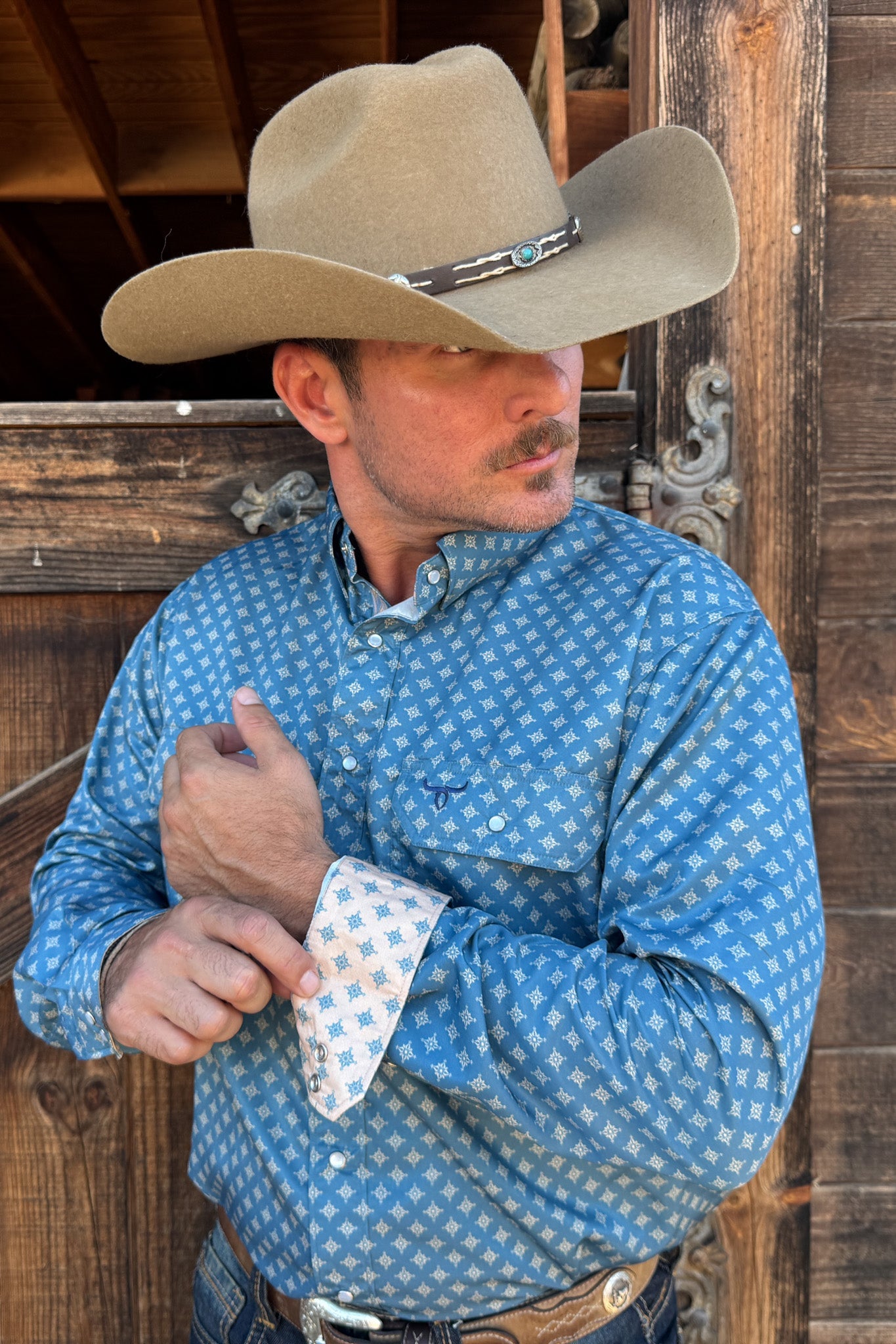 Man wearing a cowboy hat and blue patterned shirt against a wooden background