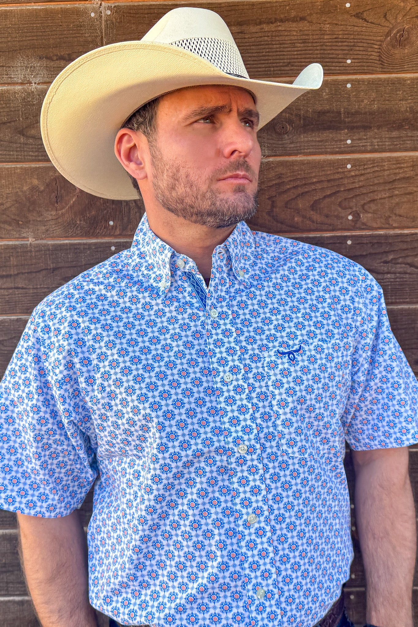 Man wearing a blue patterned shirt and cowboy hat against a wooden background