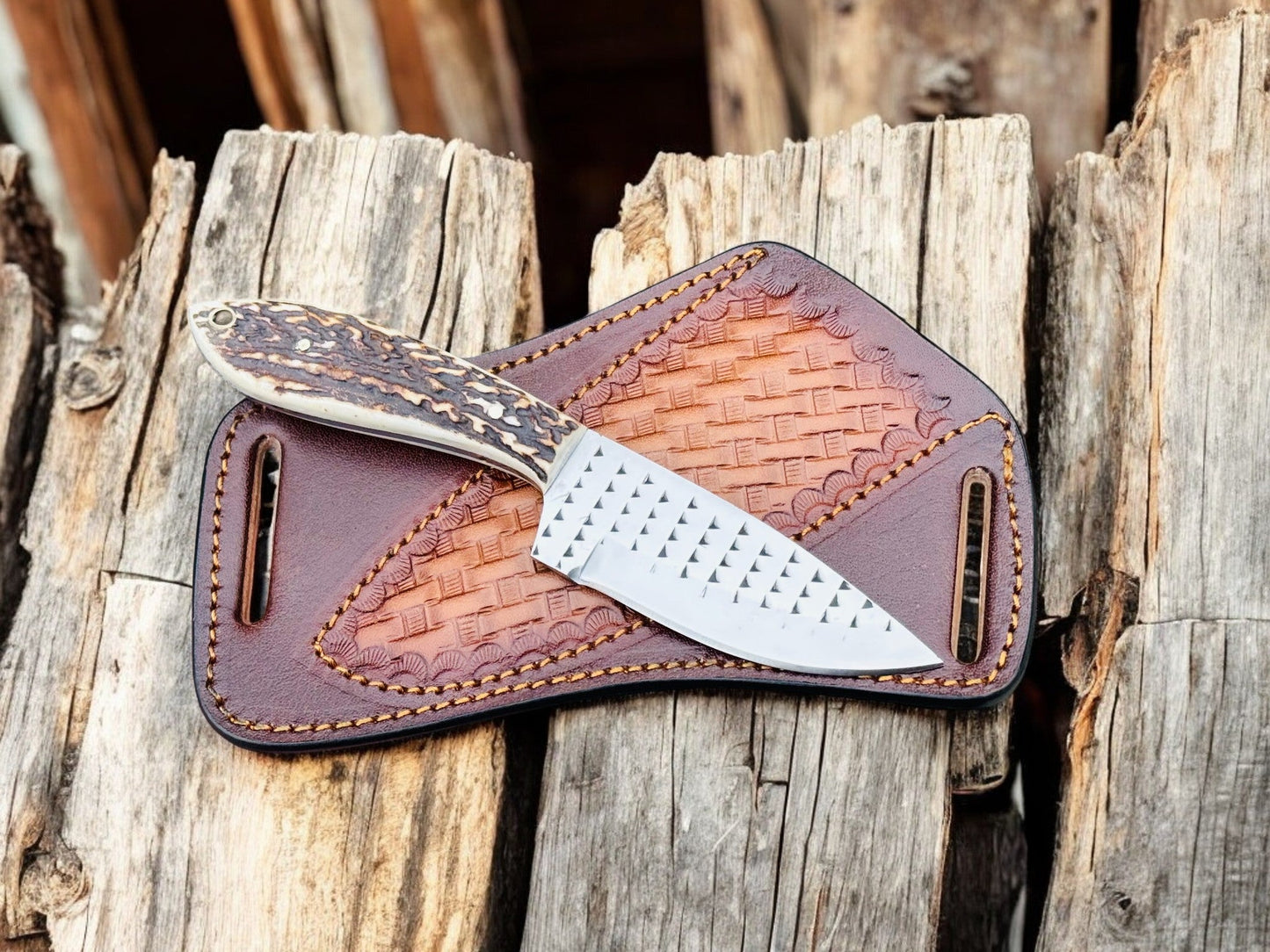 "Handmade cowboy knife with a steel blade and antler handle, resting on a textured leather sheath with woven design."