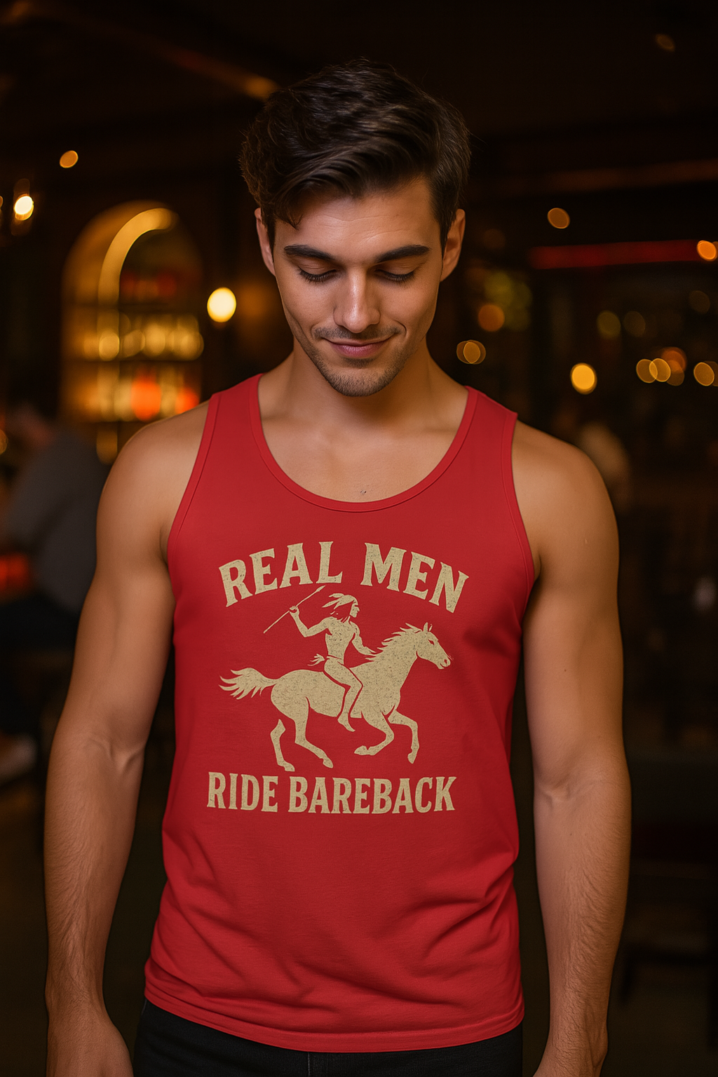 Man wearing a red tank top with a graphic and Real Men Ride Bareback text in a dimly lit setting