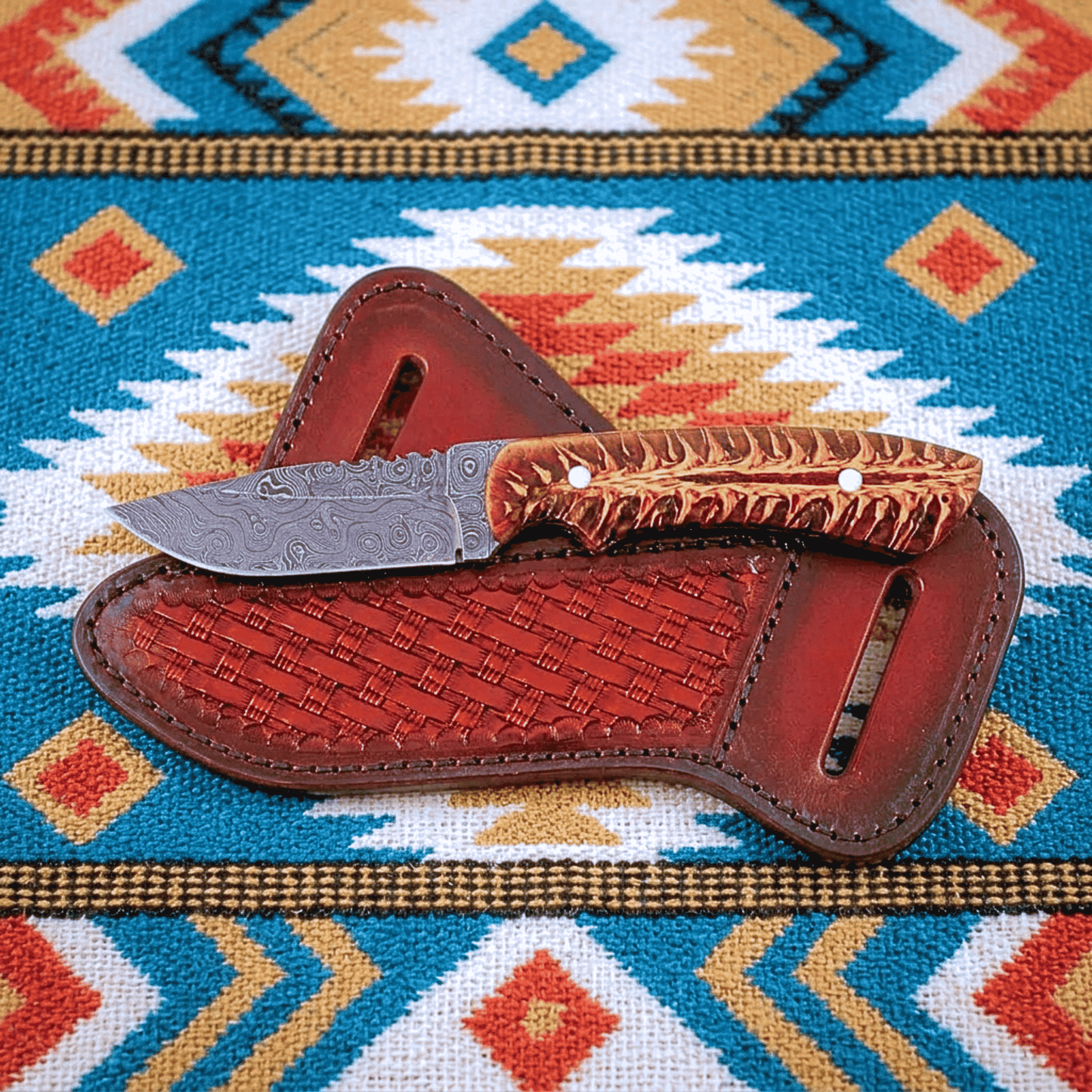 Red Mesa western fixed-blade knife with a patterned steel blade and pine cone handle rests on a basket weave brown leather sheath over a colorful geometric western blanket