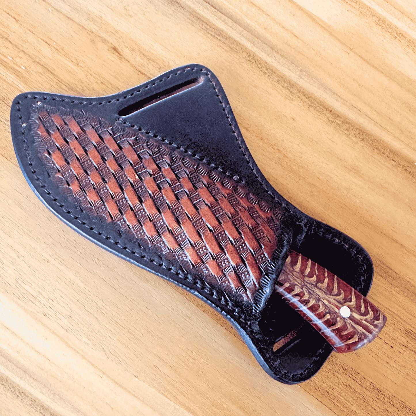 A handcrafted leather knife sheath with an embossed basketweave pattern, shown on a light wood grain background.