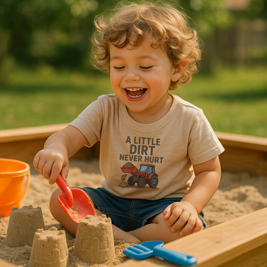 Child playing in a sandbox with sand toys, wearing a shirt with a tractor graphic and text.