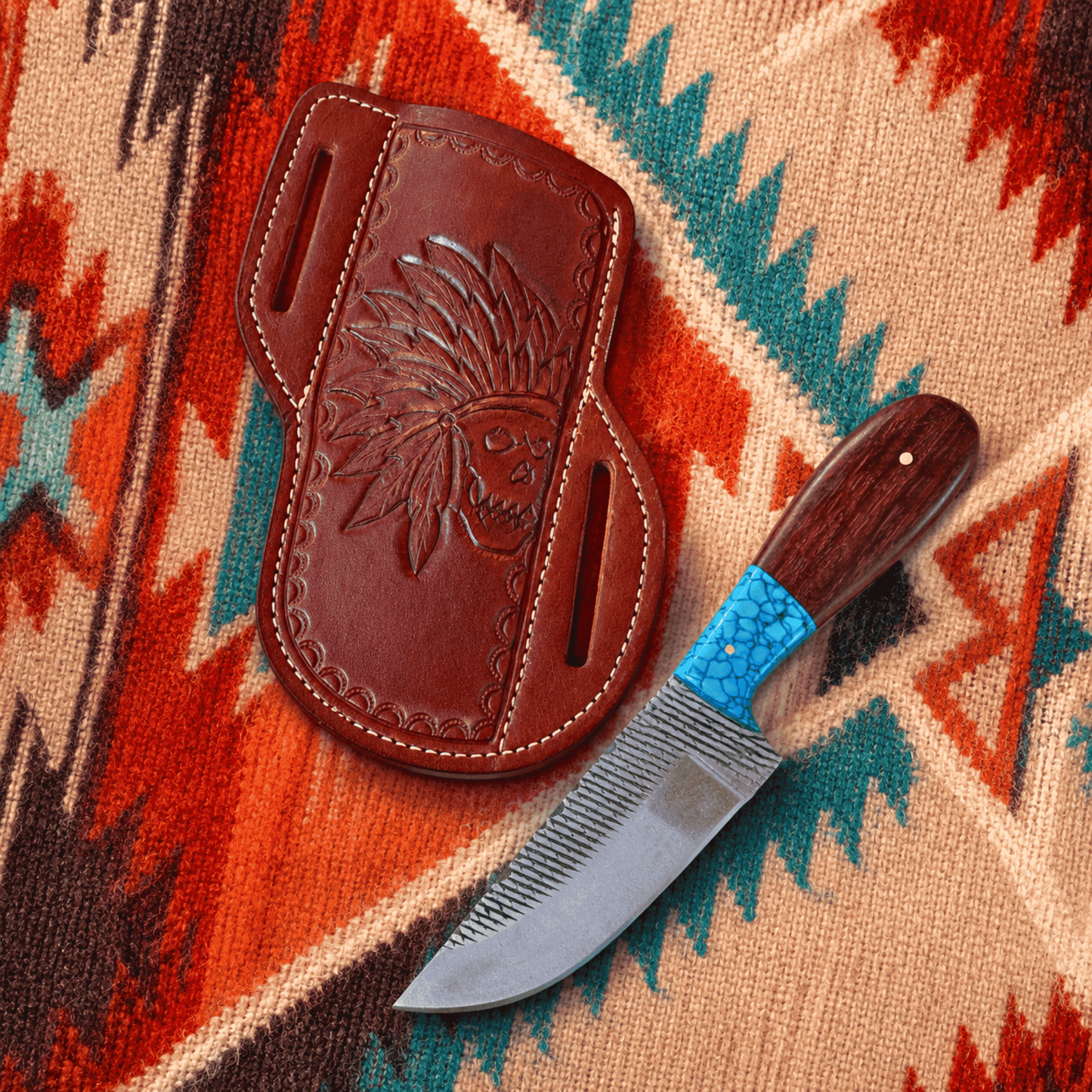 A handcrafted knife with a textured silver blade, dark wood handle, and turquoise inlay, displayed next to its brown leather sheath featuring an embossed Native American headdress design, set on a colorful patterned blanket.