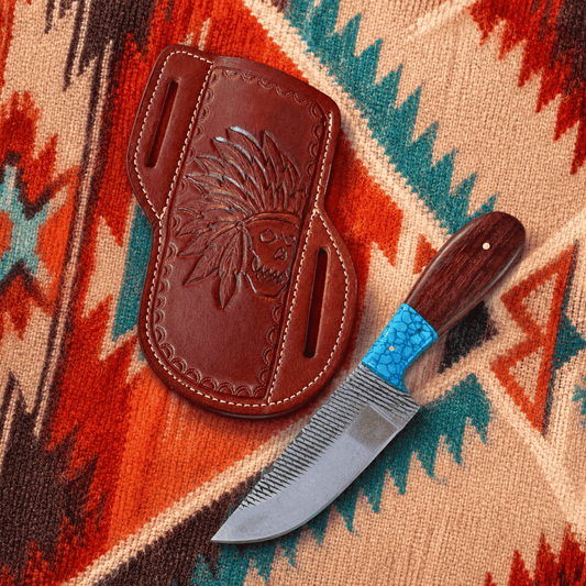 A handcrafted knife with a textured silver blade, dark wood handle, and turquoise inlay, displayed next to its brown leather sheath featuring an embossed Native American headdress design, set on a colorful patterned blanket.