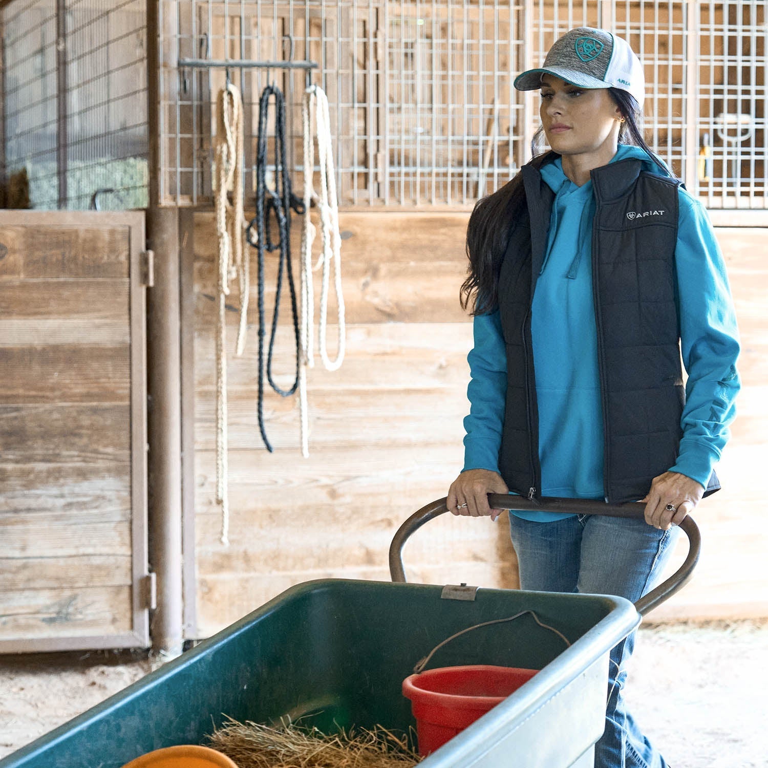 Person pushing a cart with a red bucket in a stable setting