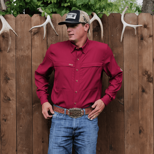 Man wearing a red shirt and blue jeans standing against a wooden fence with antlers.