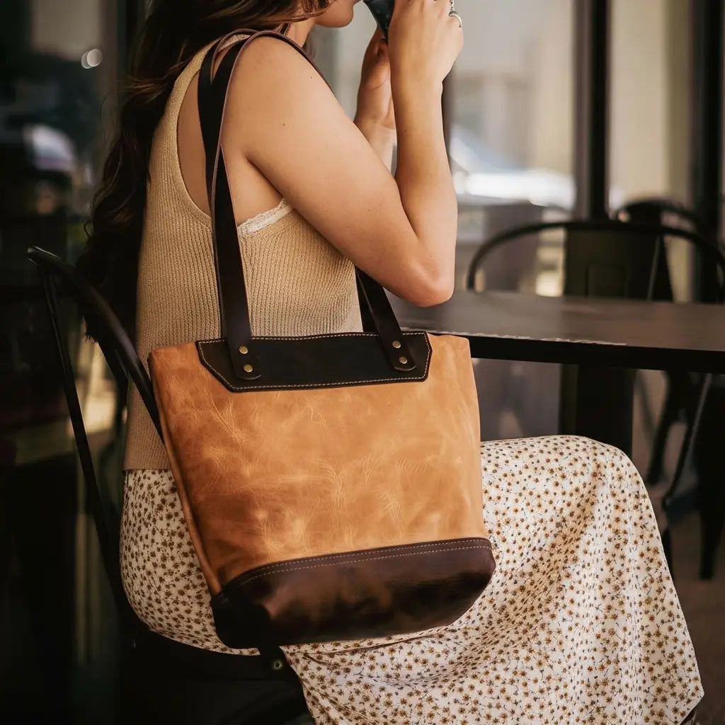 Woman sitting at a table with a brown leather handbag on her lap, holding a cup.